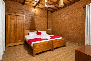 A wooden bed with a red blanket and heart pillow, a wooden wardrobe, and a ceiling fan in a room with a textured brick wall. - Vilstay Premium Panthalaza  (Narinada)