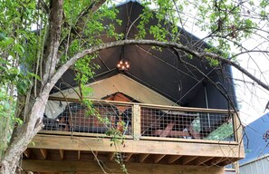 A wooden balcony with a metal railing, surrounded by trees.