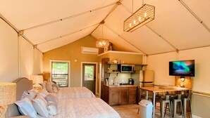 A tented accommodation with a bed, kitchenette, dining area, and a TV. - Luxury Tented Cabin Retreat - Fun Glamping Vacation by the Water for the Whole Family in Seguin, Texas (Seguin)