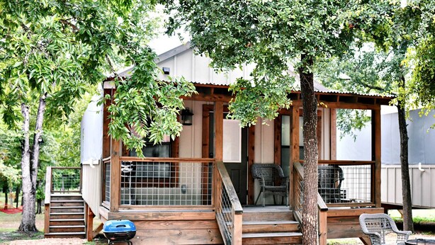 A wooden cabin with a porch, a grill, and a chair. - Luxury Tented Cabin Retreat - Fun Glamping Vacation by the Water for the Whole Family in Seguin, Texas (Seguin)
