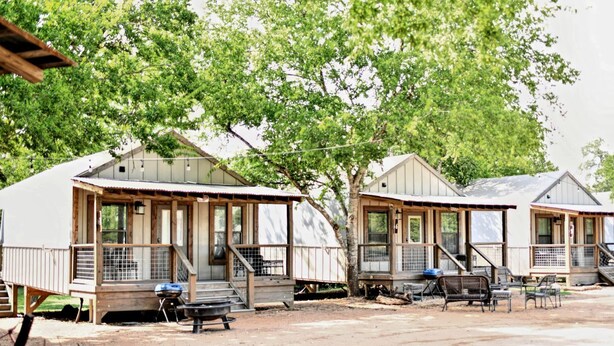 A row of mobile homes with wooden decks and steps, each with a grill and outdoor seating.
