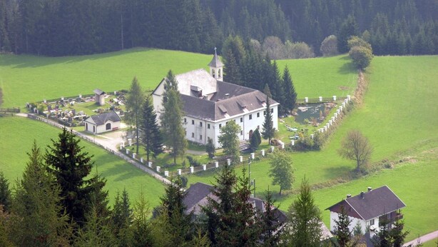 Un grand bâtiment blanc, doté d’une tour, entouré d’un cimetière et de champs verdoyants.