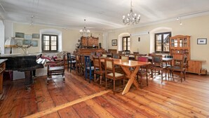 Une pièce spacieuse avec un grand piano, une table à manger en bois et des chaises, dotée de hauts plafonds et de lustres.