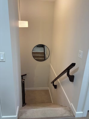 Un escalier recouvert de moquette avec une main courante, un miroir rond accroché au mur et un luminaire au-dessus.