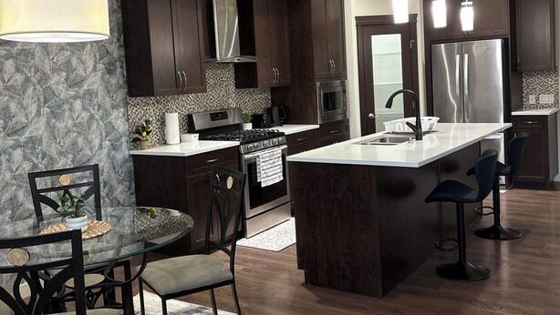 Cocina moderna con alacenas de madera oscura, electrodomésticos de acero inoxidable y una isla central con taburetes de bar.