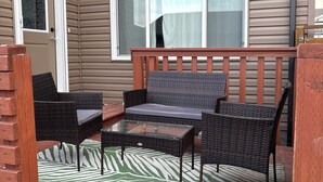 Un patio cubierto con mobiliario de mimbre, una mesa de vidrio y un tapete a rayas.