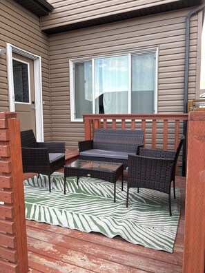 Eine überdachte Terrasse mit Korbmöbeln, einem Glastisch und einem Streifenmuster-Teppich.