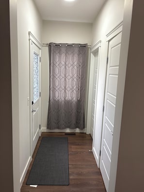 Un couloir étroit, orné d’un rideau à motifs, avec un paillasson à l’entrée et des portes blanches.
