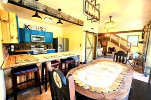 A rustic kitchen with wooden cabinets, a central island, and a dining area with a round table.
