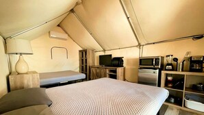 A tented room with a bed, a small desk, a television, a microwave, and a coffee maker.