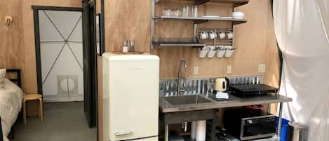 A compact kitchenette with a refrigerator, sink, and shelves for dishes.