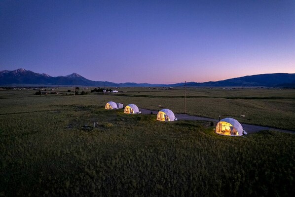 A series of dome-shaped tents in a rural landscape with mountains in the background.
