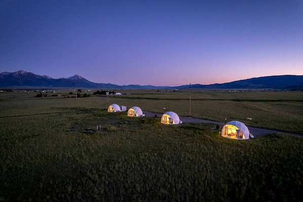 A series of dome-shaped tents in a rural landscape with mountains in the background.