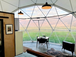 A geodesic dome room with a table and chairs, a hanging light fixture, and a view of a green landscape.