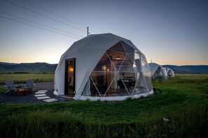 A geodesic dome structure with a fire pit and seating area in a grassy field. - Luxury Montana Dome Retreat with Breathtaking Views Near Yellowstone National Park, Montana (Park County)