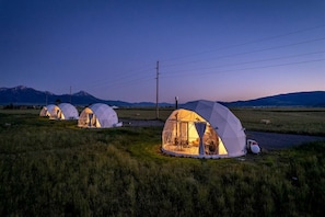 Des tentes en forme de dôme géodésique se dressent dans un champ verdoyant, avec des montagnes en arrière-plan.