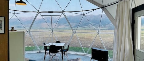 Una habitación cúpula geodésica con una mesa, sillas, un sofá y vistas al paisaje.