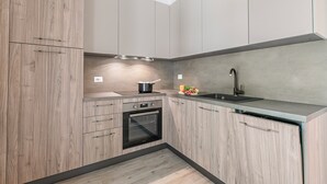 A modern kitchen with wooden cabinets, a built-in oven, a sink, and a countertop with a pot and vegetables. - Porto Letizia Napoli 2, Porlezza, Italy (Porlezza)