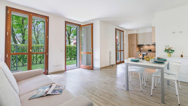 A modern living room with a sofa, a dining table with chairs, and large glass doors leading to a garden. - Porto Letizia Napoli 2, Porlezza, Italy (Porlezza)
