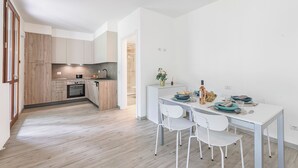 A modern kitchen with wooden cabinets, a dining area with white chairs, and a small island with a sink and a vase of flowers. - Porto Letizia Napoli 2, Porlezza, Italy (Porlezza)