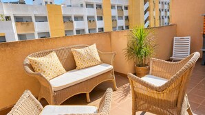 A balcony with wicker furniture, a potted plant, and a view of buildings in the background. - Orihuela Costa Relax & Sea (Alicante)