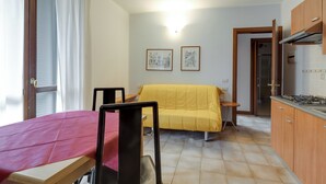 Una camera compatta con un letto, un tavolino, una sedia, un divano, un angolo cottura e due quadri appesi al muro.