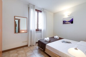 A hotel room with a bed, a bedside lamp, a window with curtains, a wall-mounted mirror, and a painting. - Porto Letizia Leoncavallo 6, Porlezza, Italy (Porlezza)