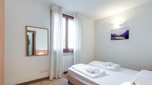 Ein Hotelzimmer mit Bett, Nachttischlampe, einem Fenster mit Vorhängen, einem Wandspiegel und einem Gemälde.