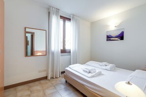 Ein Hotelzimmer mit Bett, Nachttischlampe, einem Fenster mit Vorhängen, einem Wandspiegel und einem Gemälde.