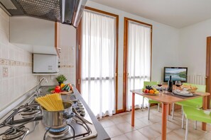 Una cuina moderna amb fogó a gas, un plat de spaghetti i una zona de menjador amb taula preparada per a dues persones.