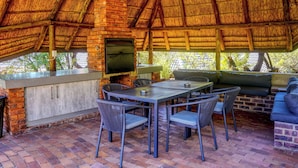 Un patio al aire libre con chimenea de ladrillo, una mesa con sillas y un área de estar con cojines.