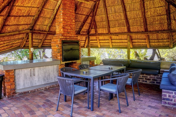An outdoor patio with a brick fireplace, a table with chairs, and a cushioned seating area.