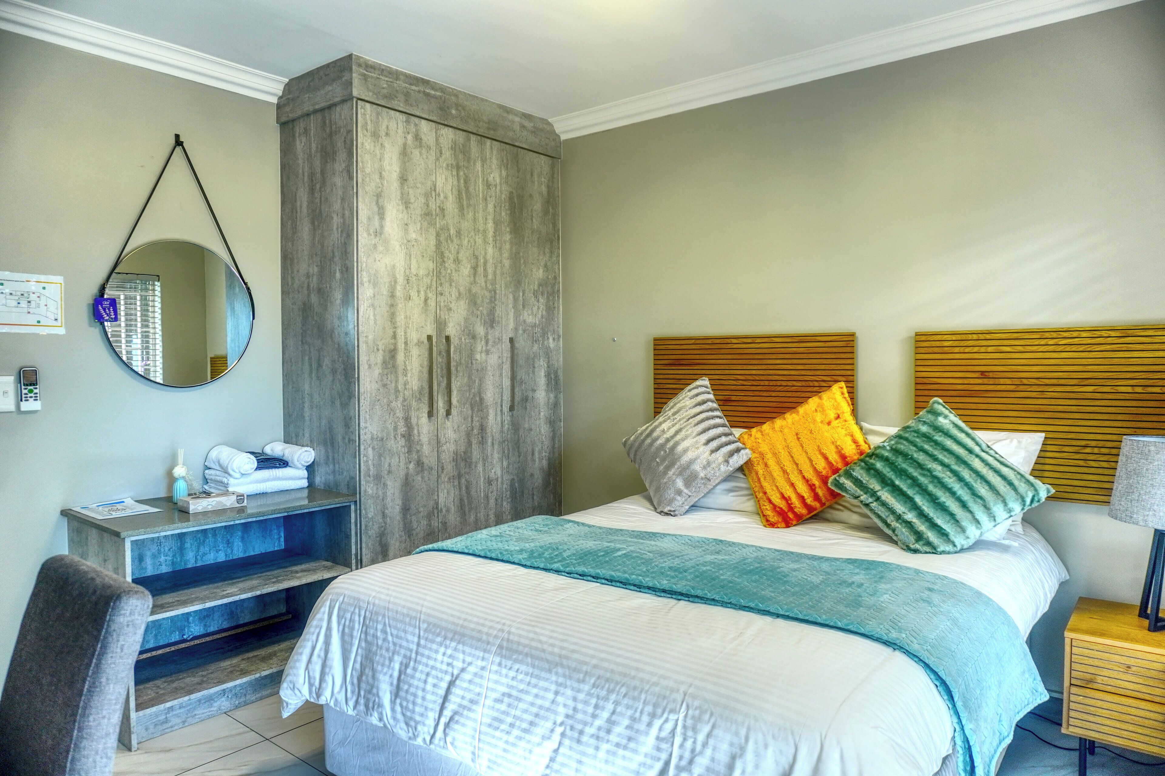 A hotel room with a bed, a desk, a chair, a mirror, and a wooden headboard.