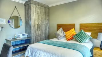 Une chambre d’hôtel avec un lit, un bureau, une chaise, un miroir et une tête de lit en bois.