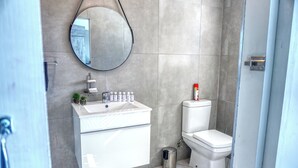 Un baño moderno con un lavamanos blanco, un inodoro y un espejo redondo.