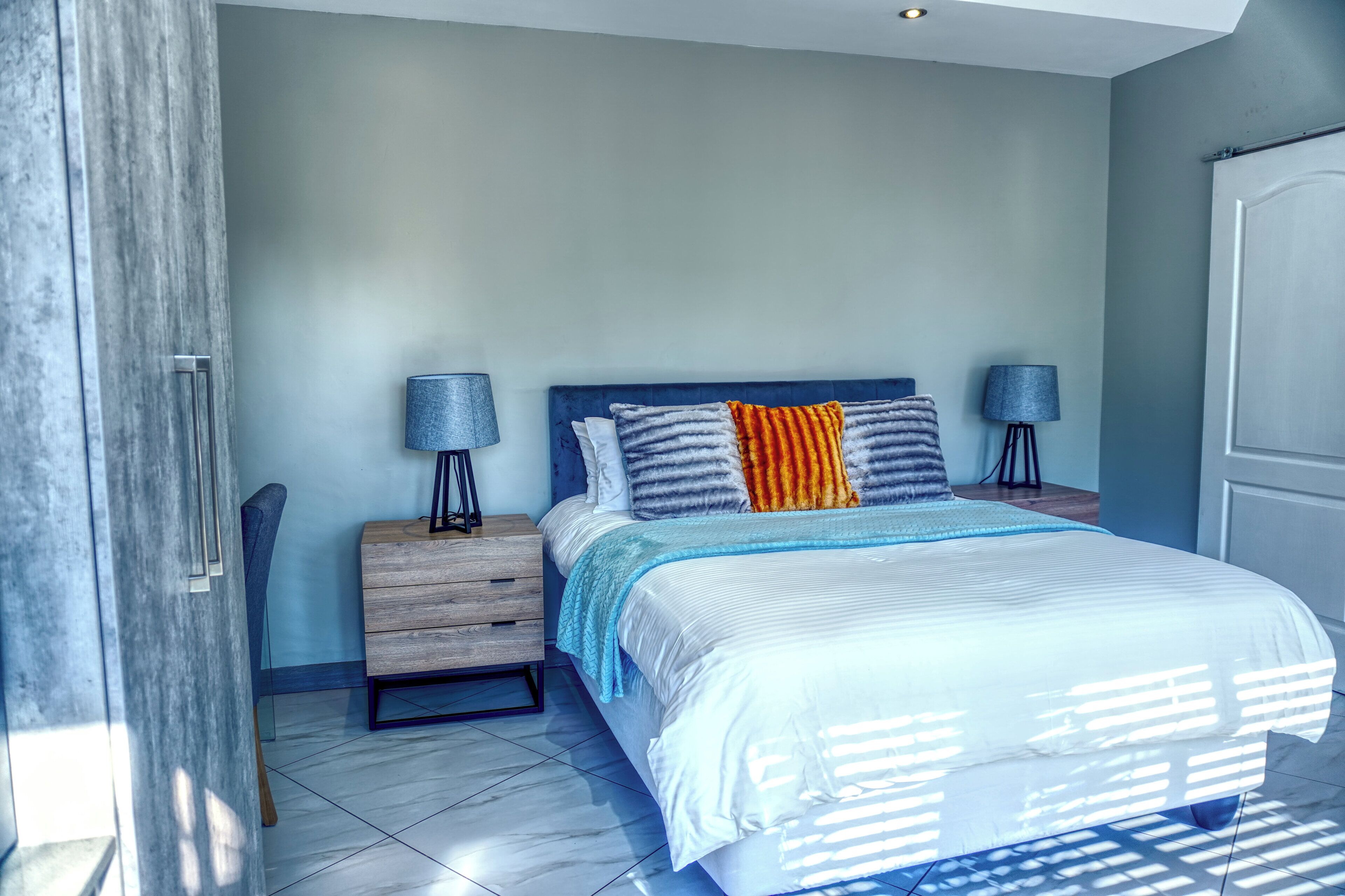 A bedroom with a bed, two bedside tables, a nightstand, a chair, and a door.