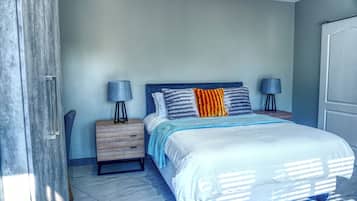 A bedroom with a bed, two bedside tables, a nightstand, a chair, and a door.