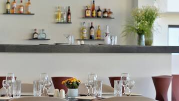 A dining table set with glasses and a vase of flowers, with shelves of bottles in the background.