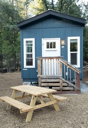 Eine kleine, blaue Holzhütte mit einer Holzterrasse und einem Picknicktisch.