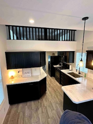 A modern kitchen with a central island, upper-level seating, and a visible staircase. - Charming Bright Tiny Home with Stargazing & Yoga Dome Near Yosemite, Groveland, California (Groveland)