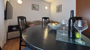 A dining area with a round table, chairs, a bowl of fruit, wine glasses, and a bottle of wine. - Charming Apartment Secret Garden (Lukoran)