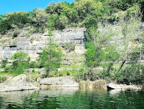 Eine natürliche Landschaft mit einer felsigen Klippe, Bäumen und einem Gewässer.