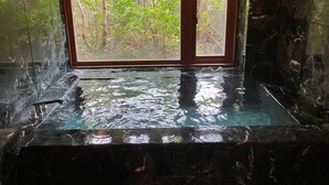 Un cuarto de spa con un amplio ventanal, una bañera de mármol y vistas a un bosque.