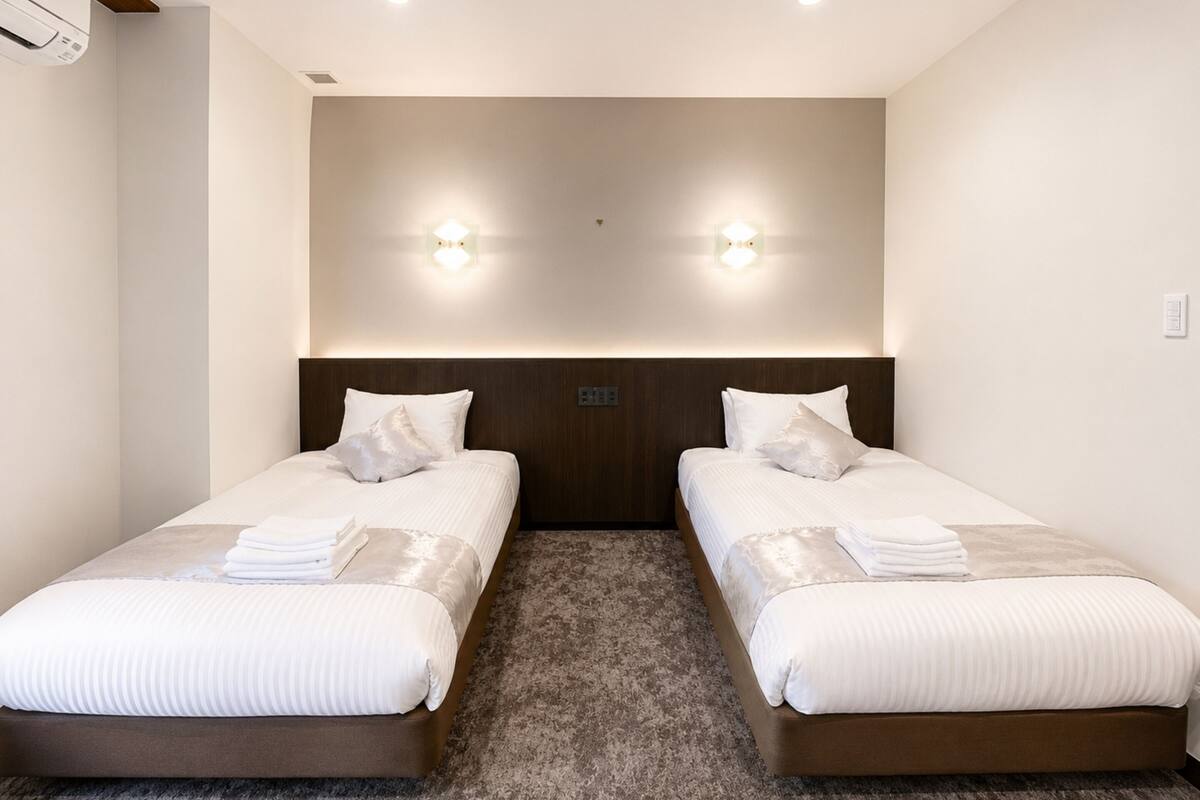Una habitación de hotel con dos camas, cabecero de madera, suelo alfombrado e iluminación en la pared.