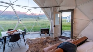 A tented room with a view of mountains, a dining table, chairs, a fur rug, and a bed.