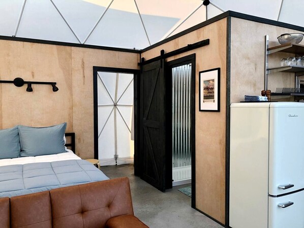 A bedroom with a bed, a chest of drawers, a white refrigerator, and a door leading to a balcony. - Montana Luxury Dome Stay with Panoramic Views Near Yellowstone National Park (Park County)