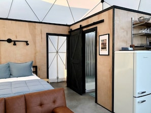 Une chambre à coucher comprenant un lit, une commode, un réfrigérateur blanc et une porte donnant sur un balcon.