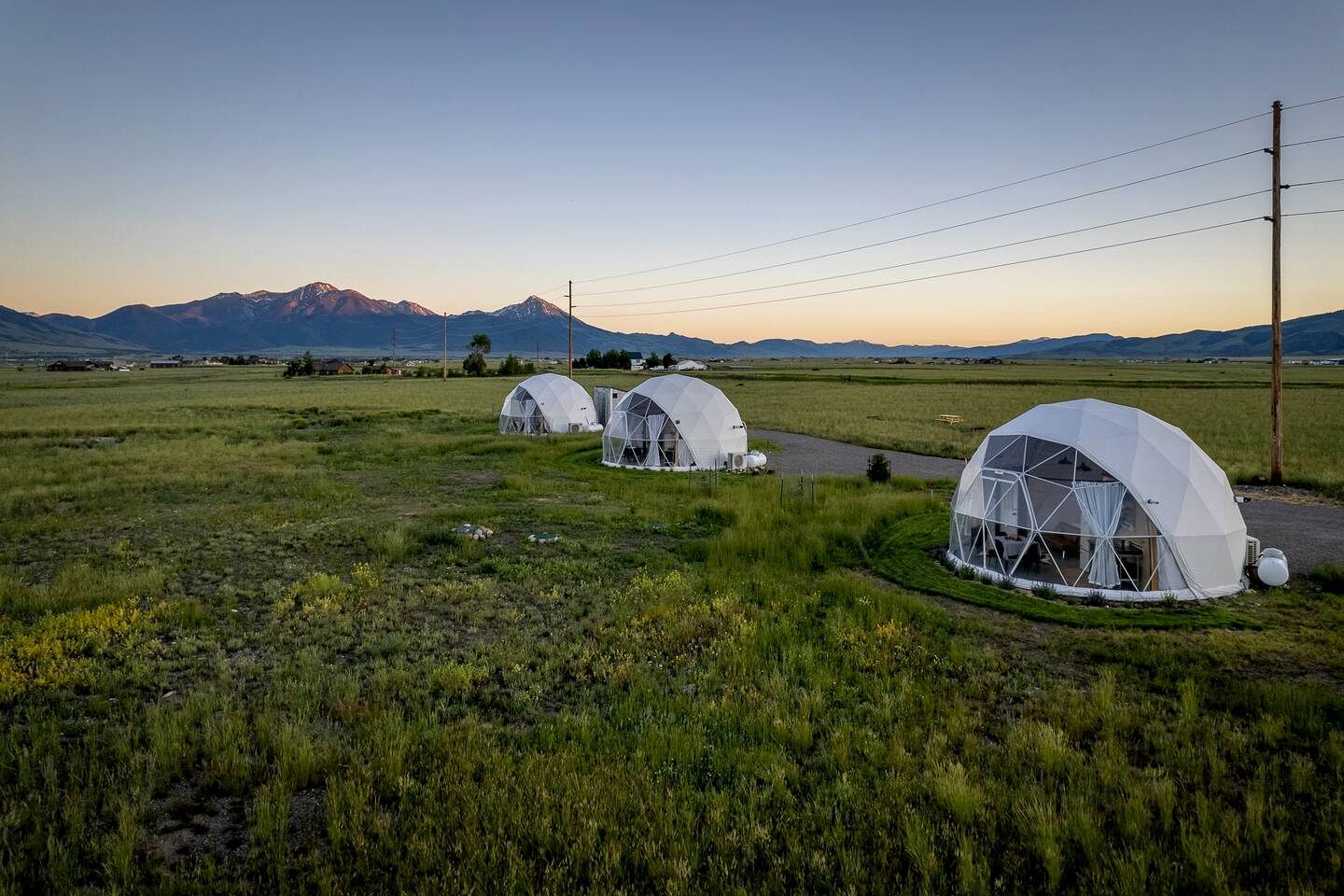 Geodesic dome structures in a rural setting with a mountain backdrop.