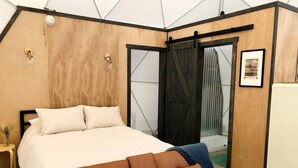A bedroom with a bed, a bench, a door, and a framed picture on the wall.
