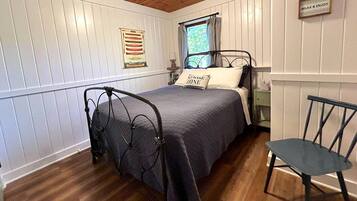 Een slaapkamer met een bed, een stoel, een raam met gordijnen, een bord aan de muur en een decoratie.